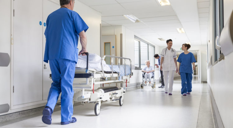 Male nurse pushing stretcher gurney bed in hospital corridor with doctors & senior female patient